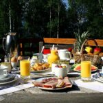 Photo d'un petit déjeuner avec jus d'orange, fruits, viennoiseries, œufs, café et charcuteries.